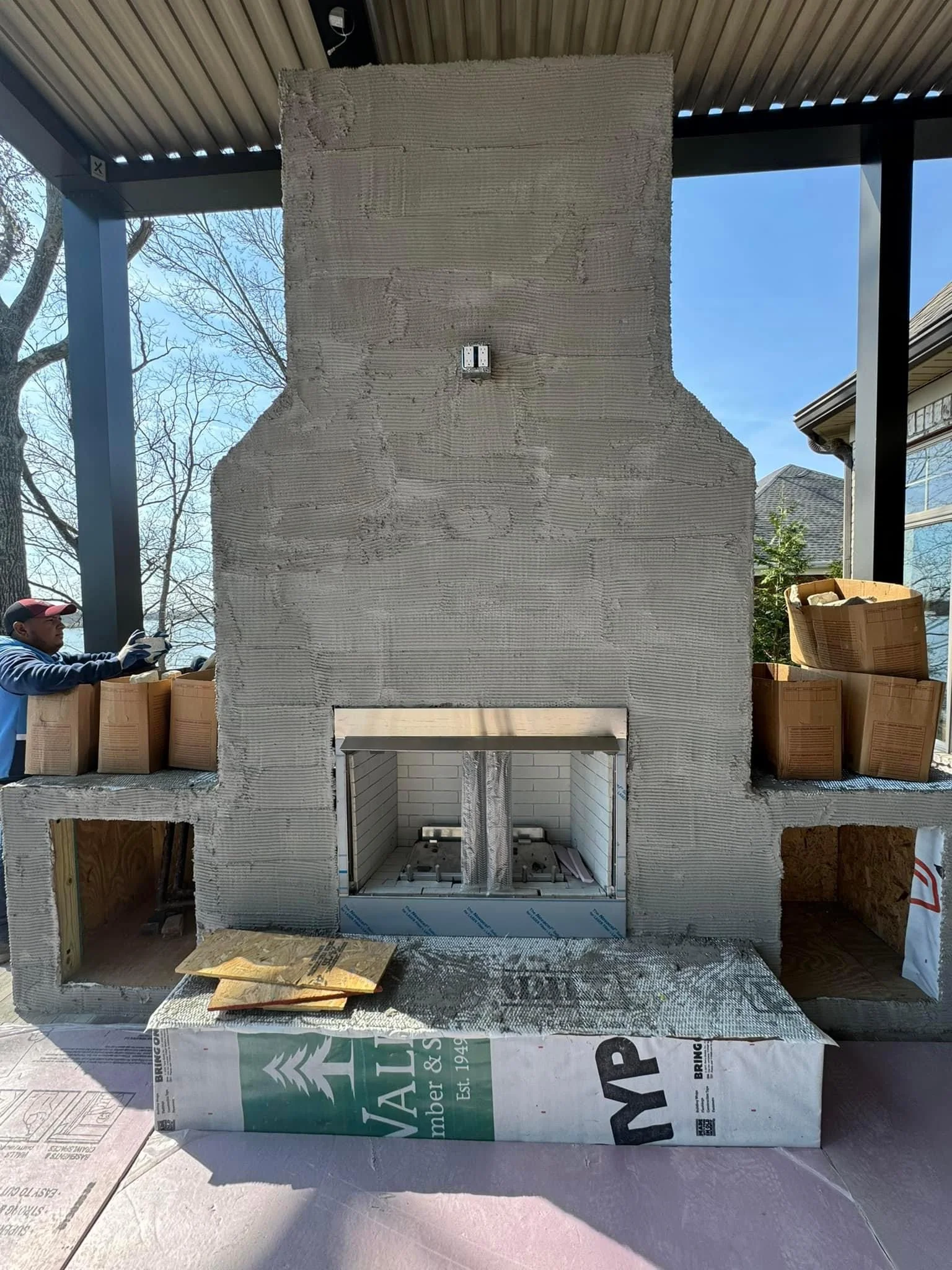 Newly constructed brick fireplace with metal firebox insert during final stages of patio installation