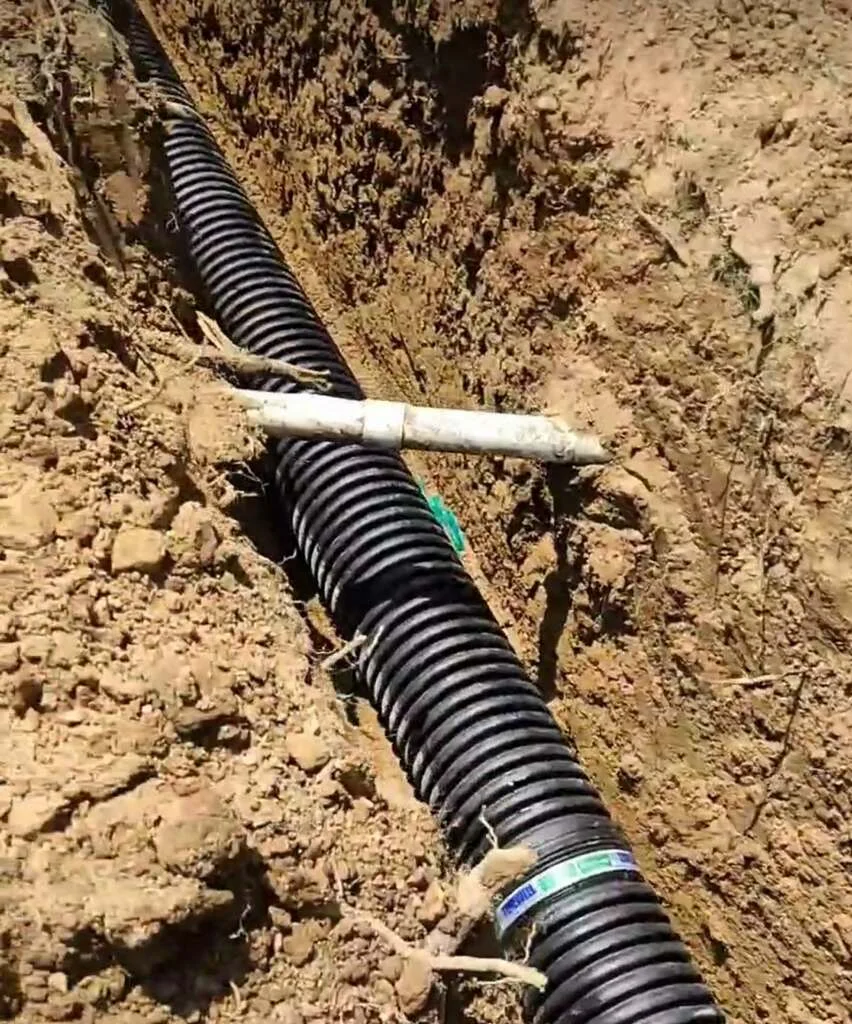 Black corrugated drain pipe installed in trench with white PVC connector and identification tape