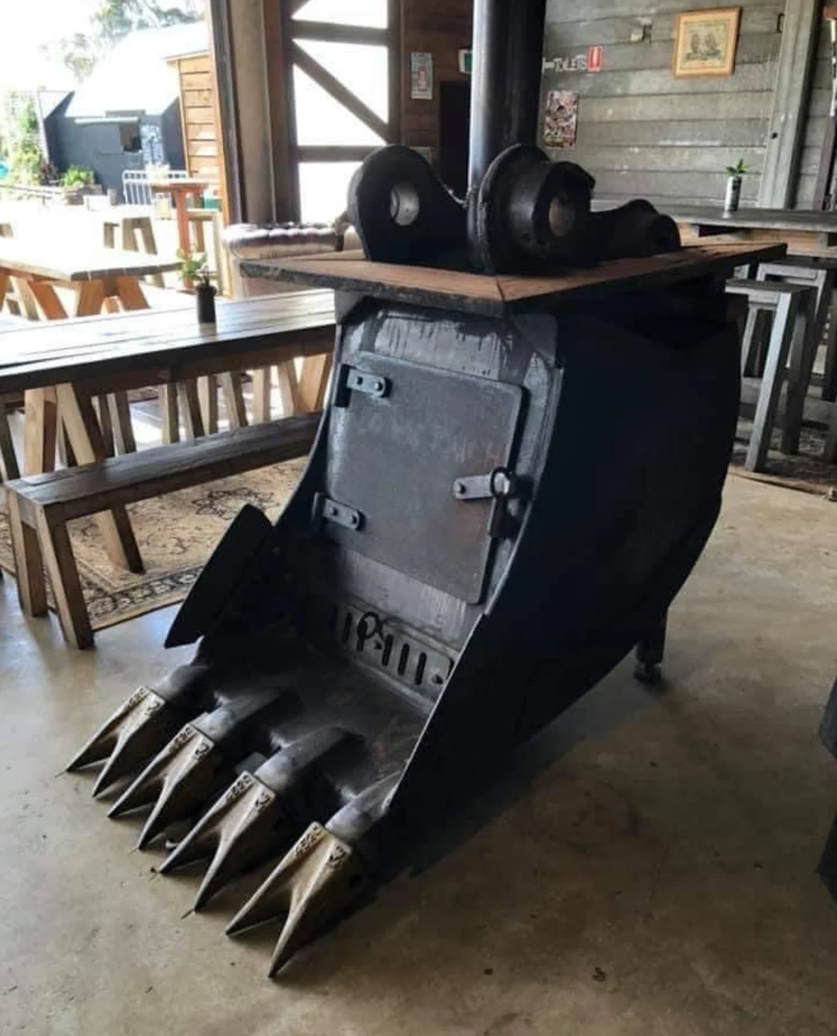 Custom black excavator bucket with dumbbell storage top and metal teeth displayed indoors