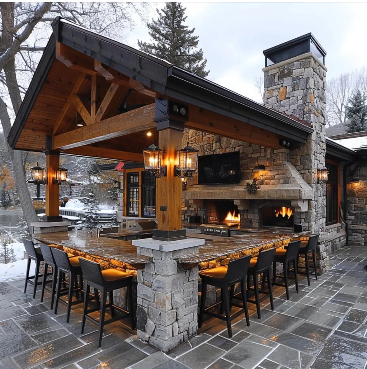 Outdoor patio with stone fireplace, timber pavilion, and bar seating in winter