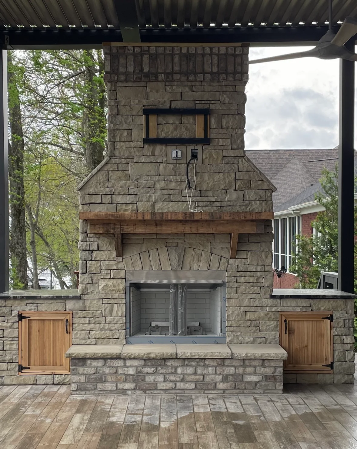Stone fireplace with pergola, wood mantel, glass doors, and cedar cabinets on composite deck
