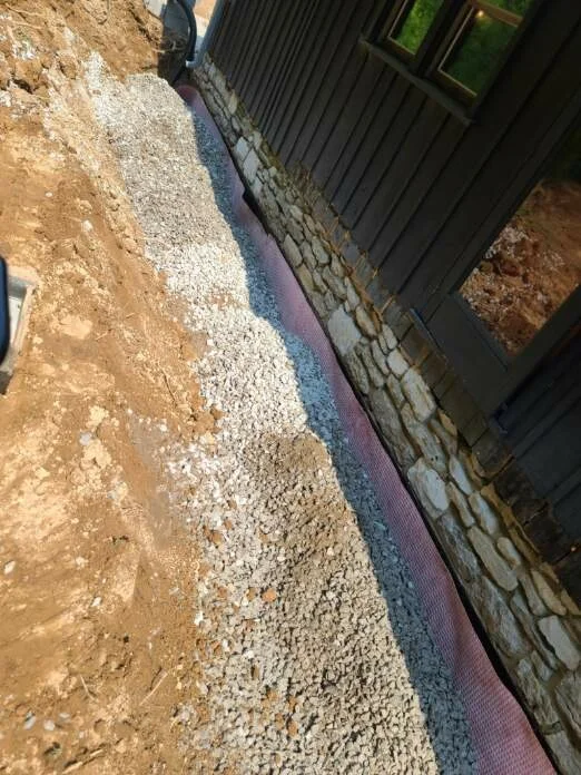 Gravel base and drainage installation along building foundation with stone retaining wall