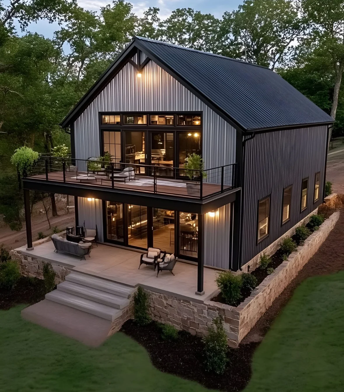 Modern two-story home addition with metal siding, black roof, and stone patio at dusk