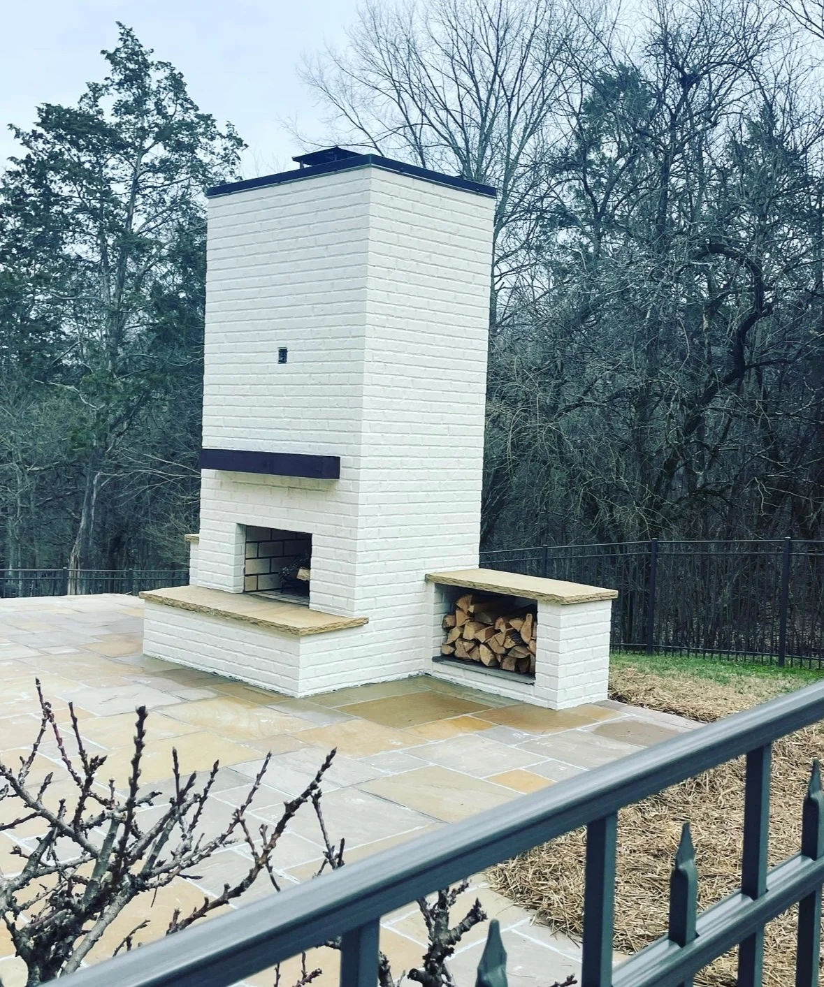 Modern white fireplace with dark roof cap and firewood storage on stone patio