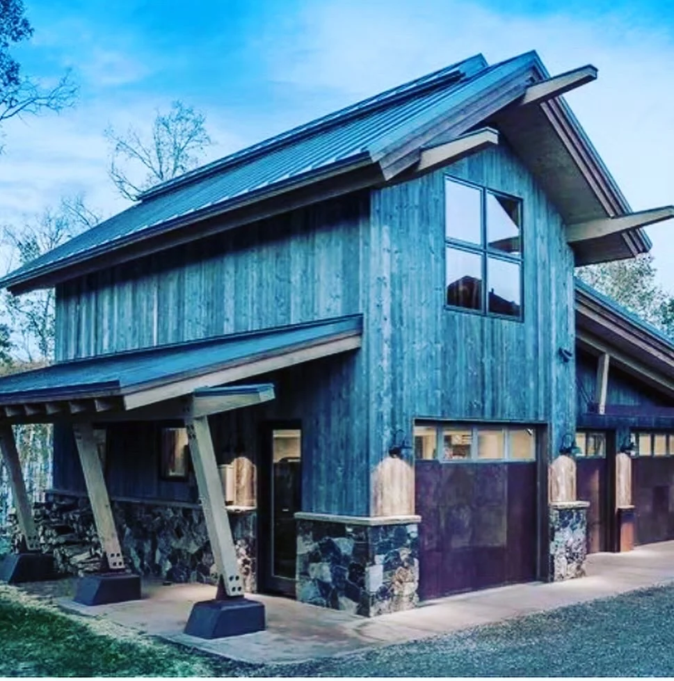 Modern barn-style home with blue metal siding, large windows, and stone foundation details