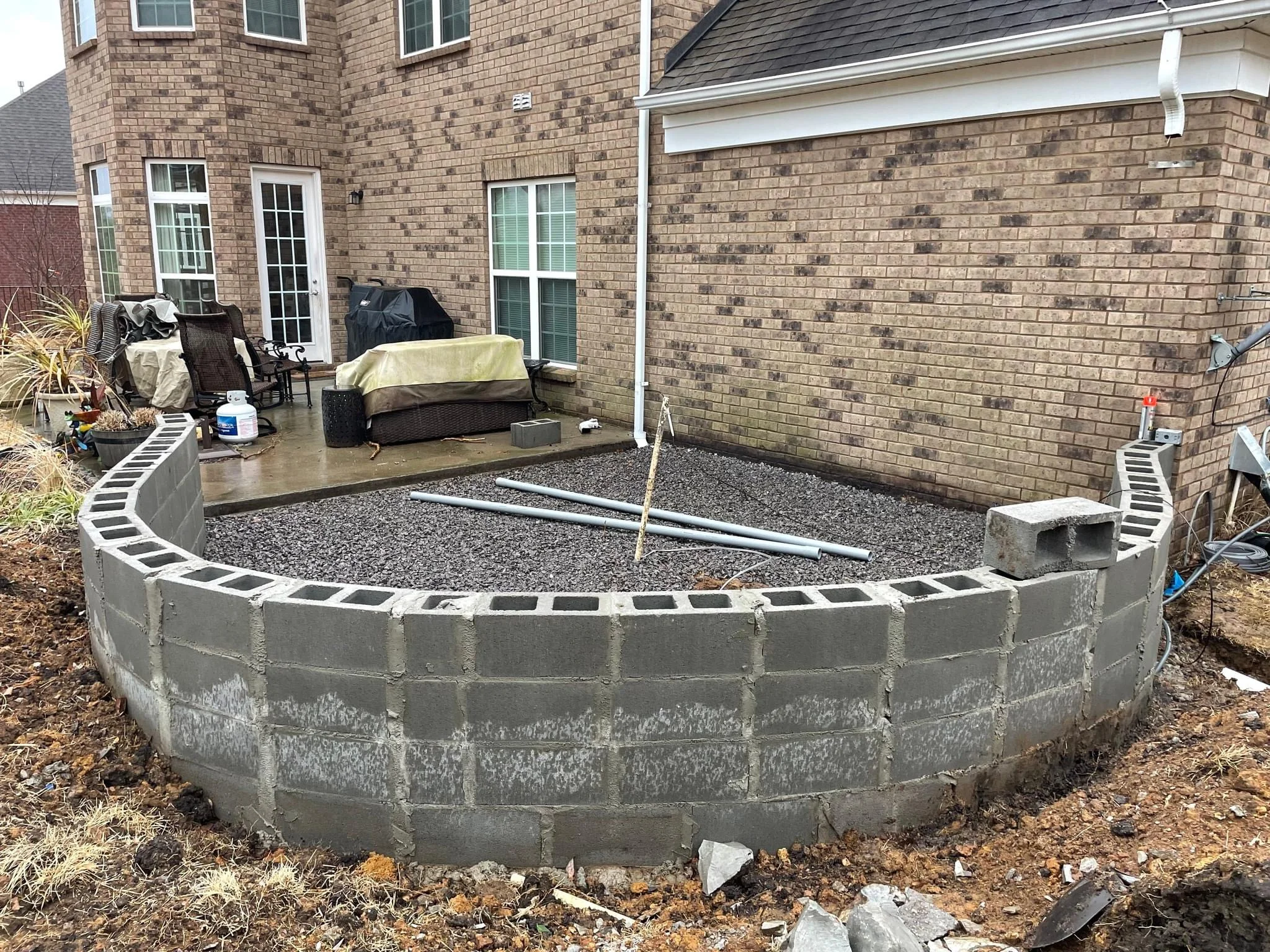 Curved concrete block retaining wall under construction with gravel fill and white cap blocks