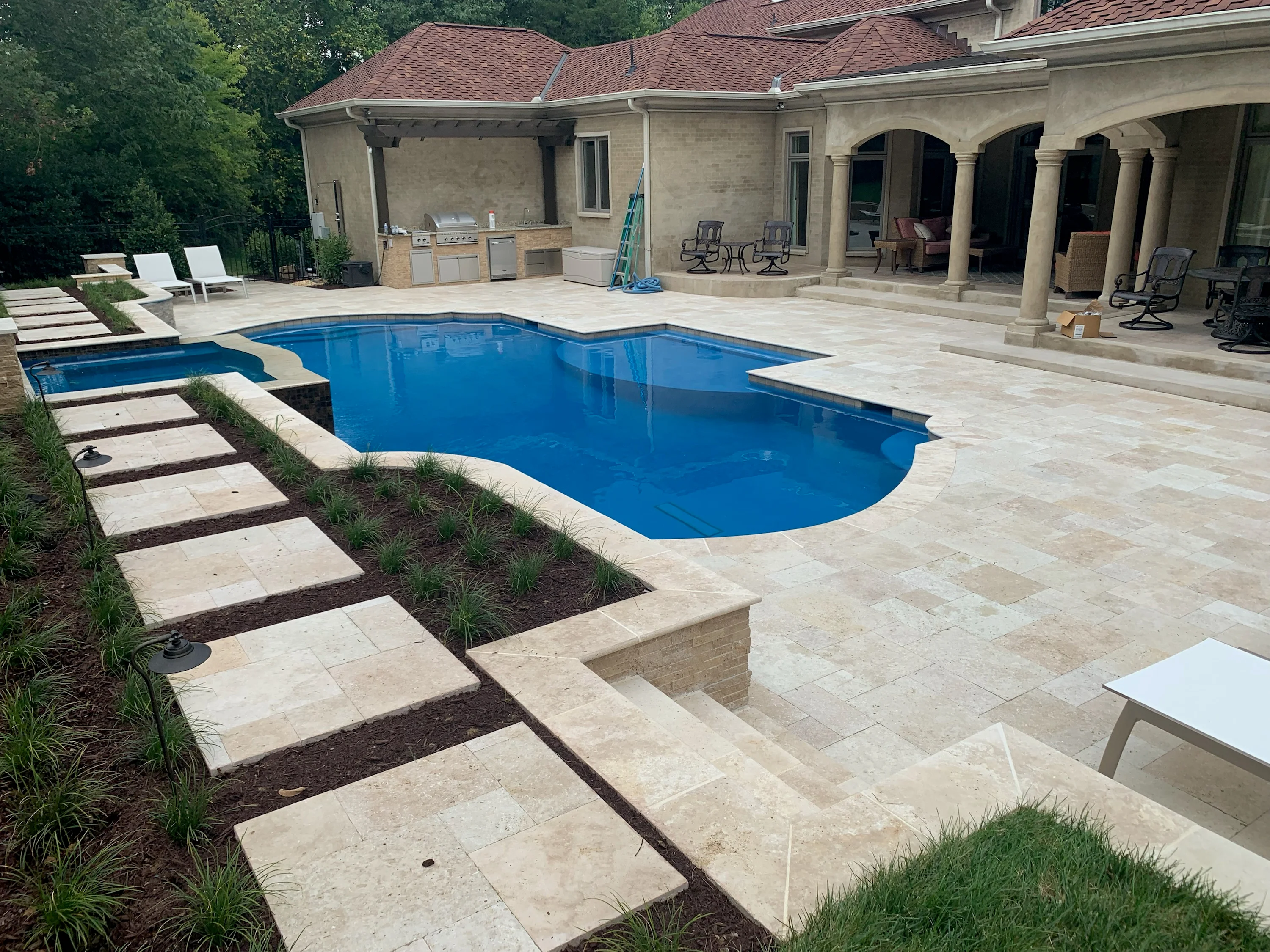 Custom in-ground pool with travertine deck and stone patio adjacent to brick home
