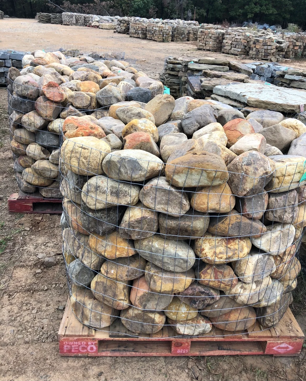 Palletized natural stone boulders in mesh wrapping, various earth tones, yard storage