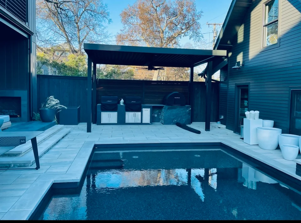 Modern backyard pool with dark water, light pavers, black pergola, and white planters