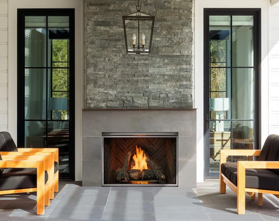 Modern outdoor patio with active fireplace, stone accent wall, and glass doors