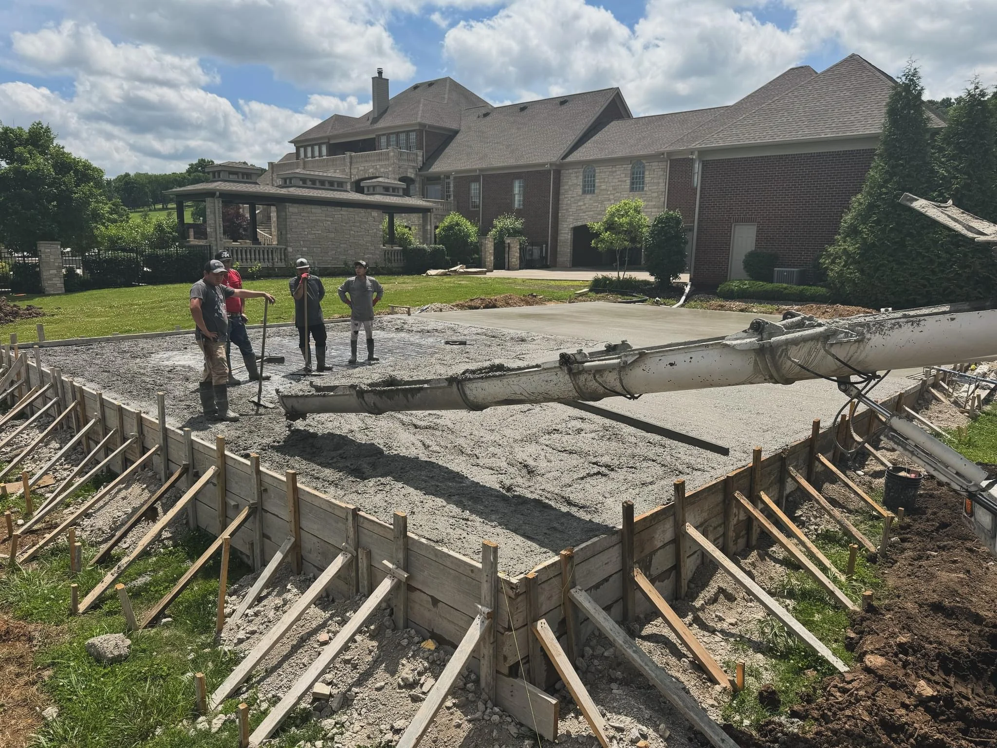 Concrete driveway installation in progress with wooden forms and crew on residential property