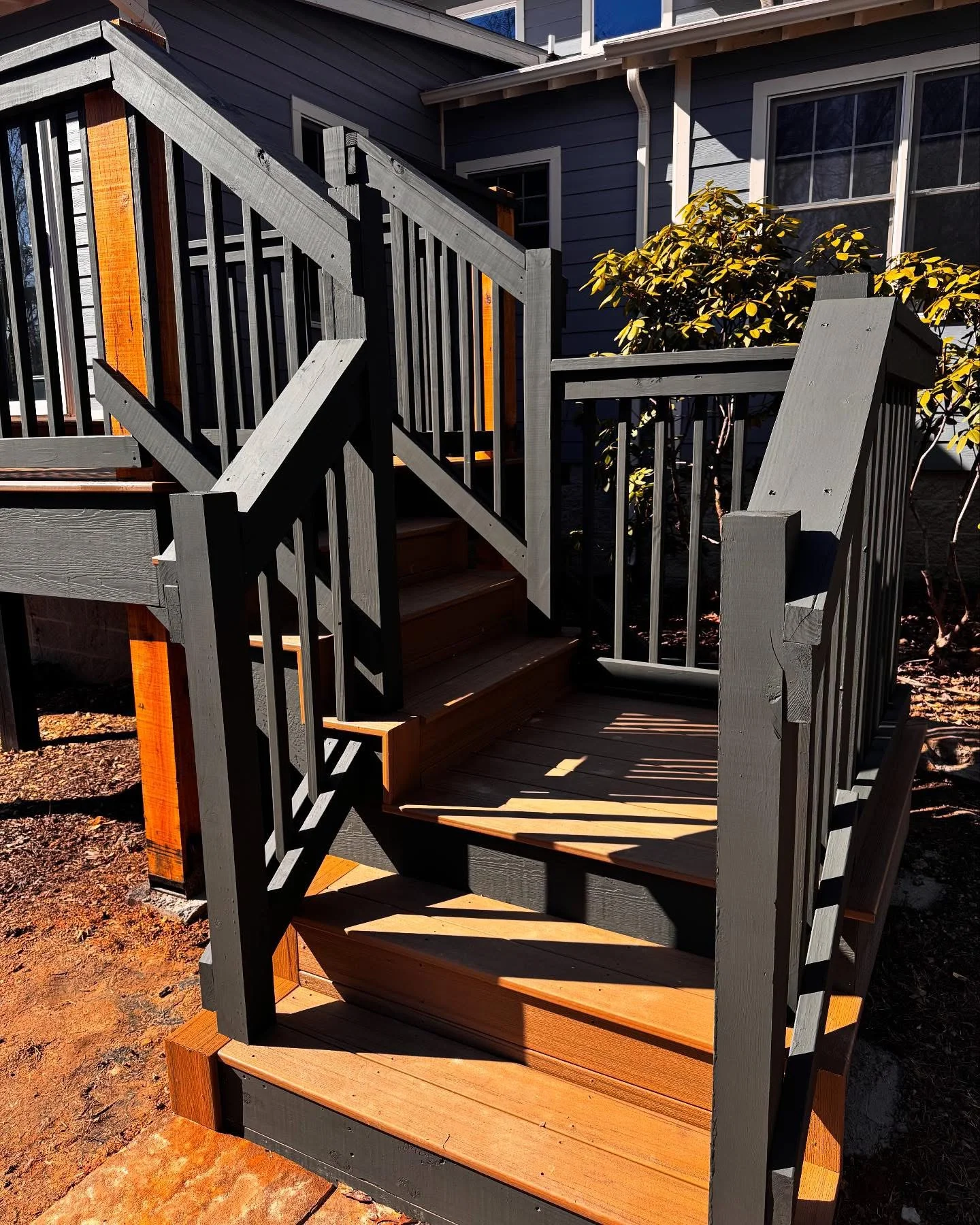 Custom wood and composite deck stairs with gray railings attached to dark blue house