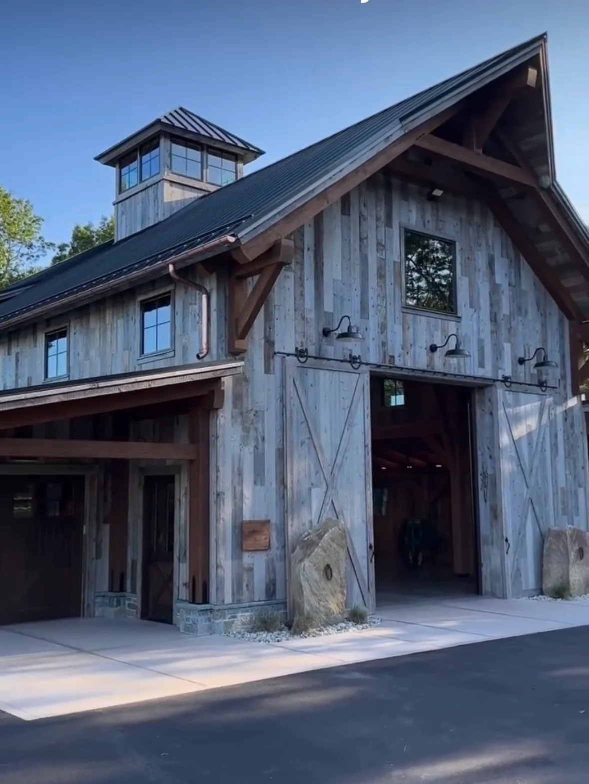 Modern barn with gray wood siding, metal roof cupola, and large black sliding doors