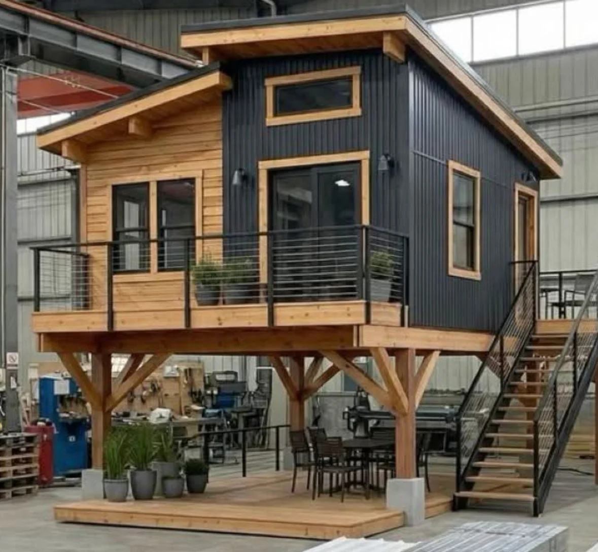 Modern elevated tiny home with wood siding, metal accents, and wraparound deck
