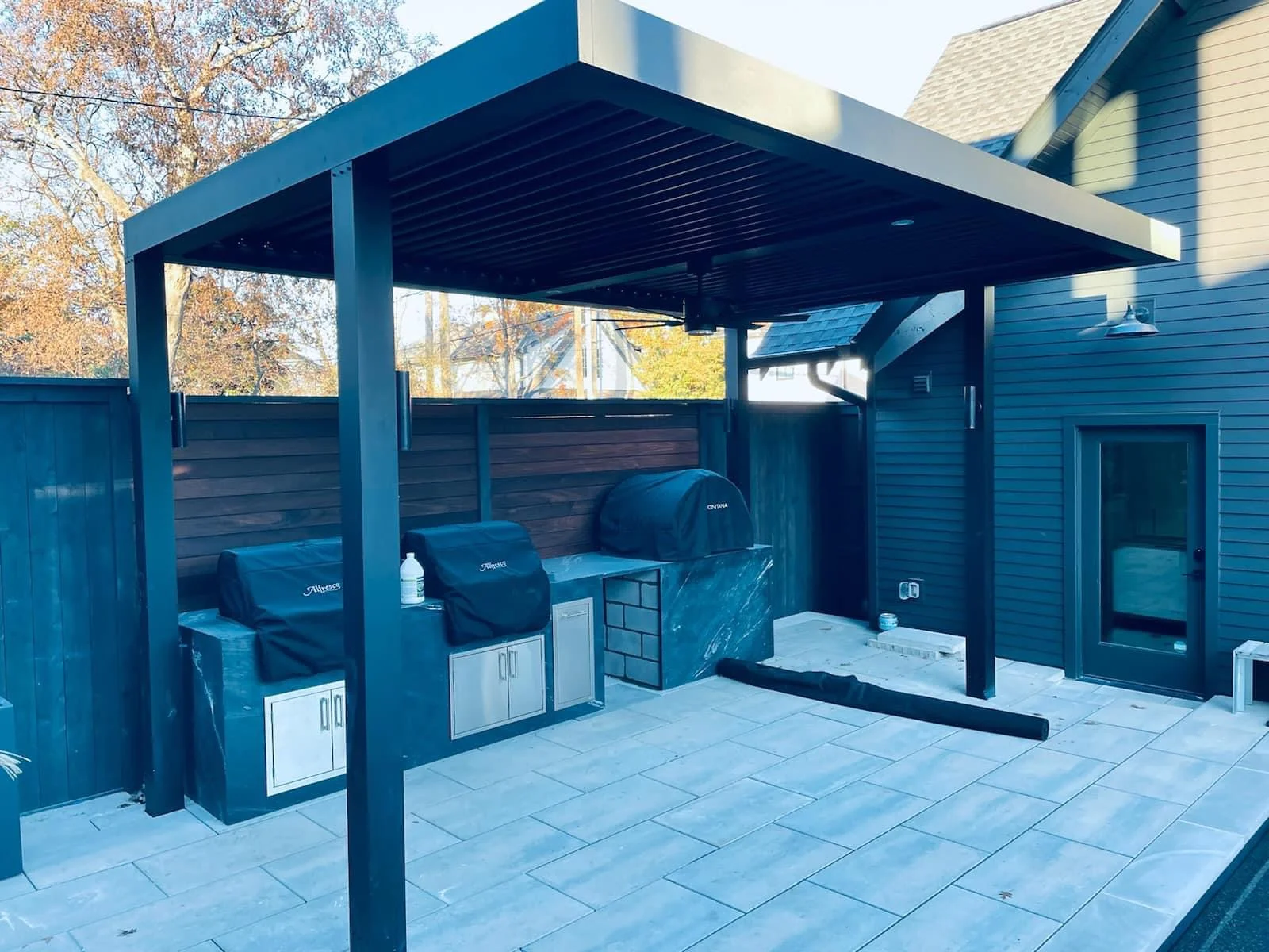 Modern blue pergola with outdoor kitchen, grills, and paver patio in residential backyard
