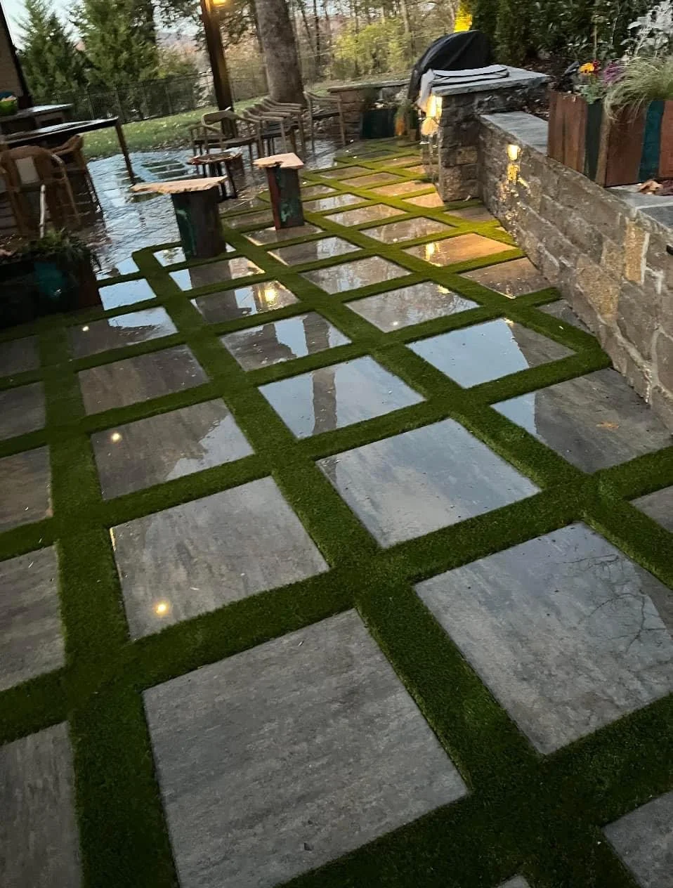Concrete paver patio with green artificial turf grid pattern and landscape lighting