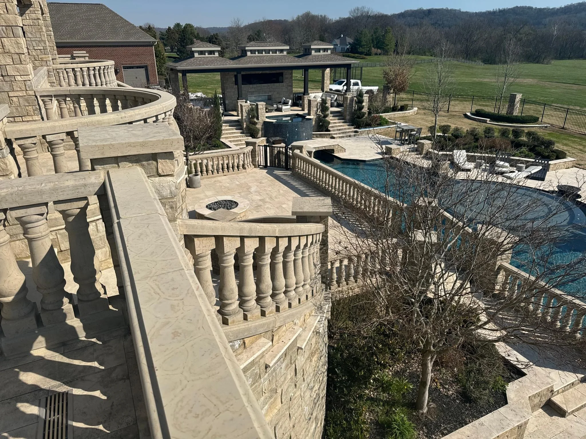 Aerial view of luxury stone patio with pool, fire pit, and covered pavilion overlooking rural landscape