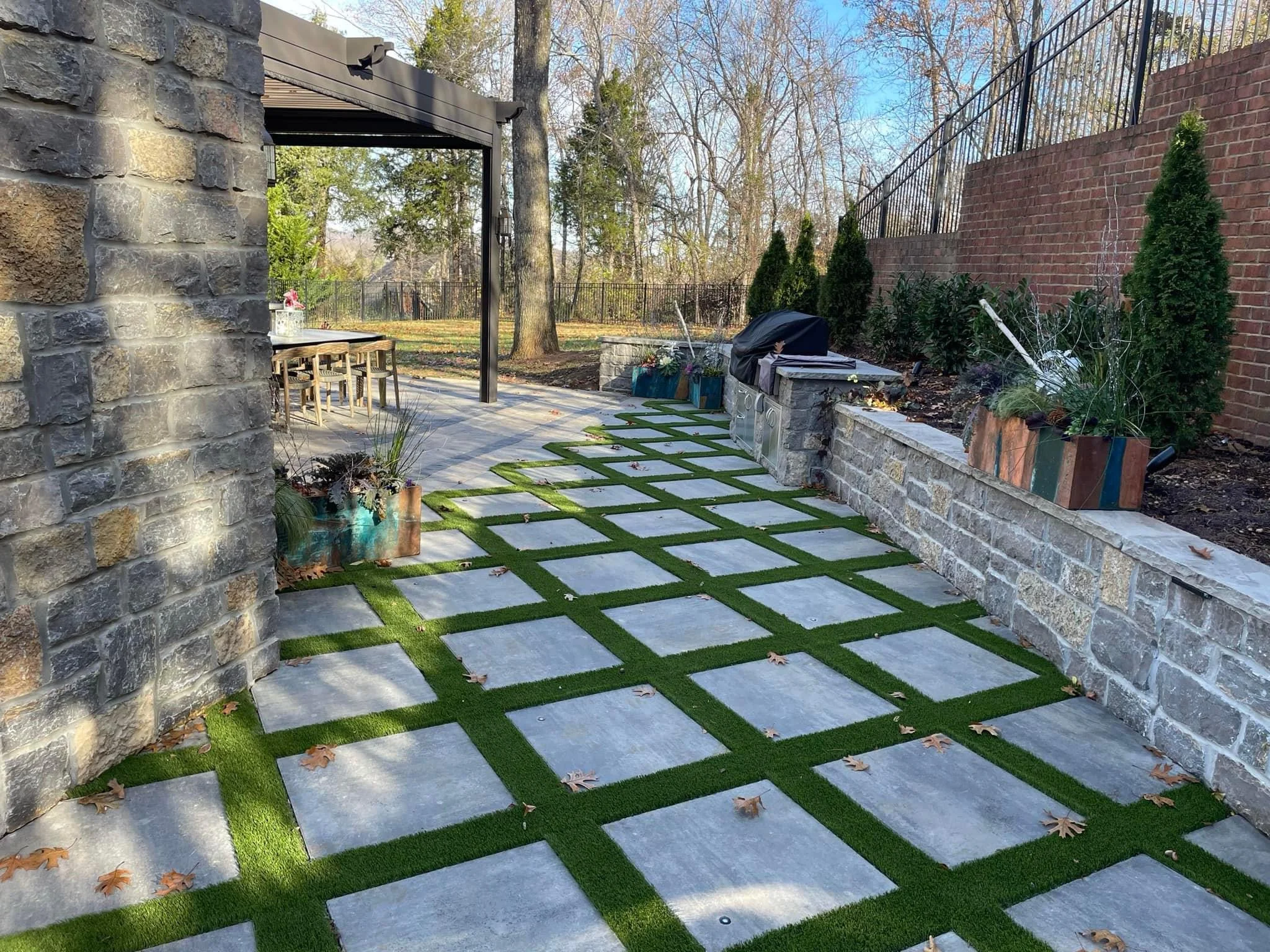 Modern patio with gray permeable pavers, green sod strips, stone walls, and pergola in Franklin