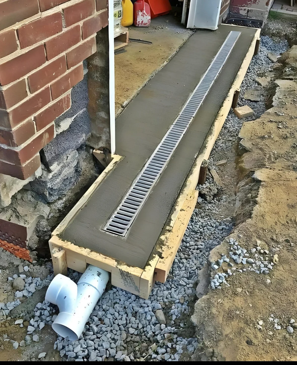 Foundation drainage system with metal grate and PVC pipe installed along brick foundation
