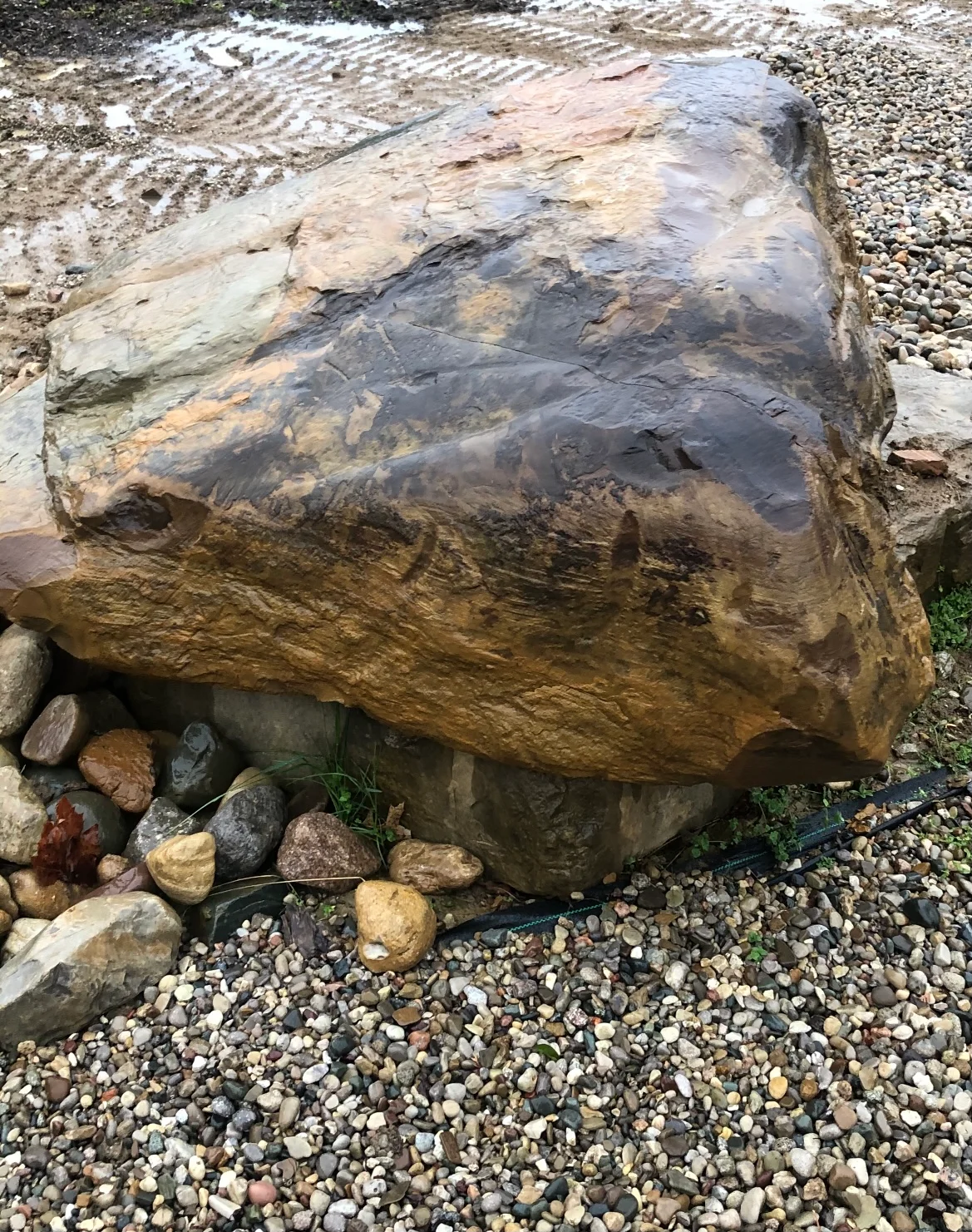 Large natural boulder installed on gravel base with landscape rocks and drainage preparation