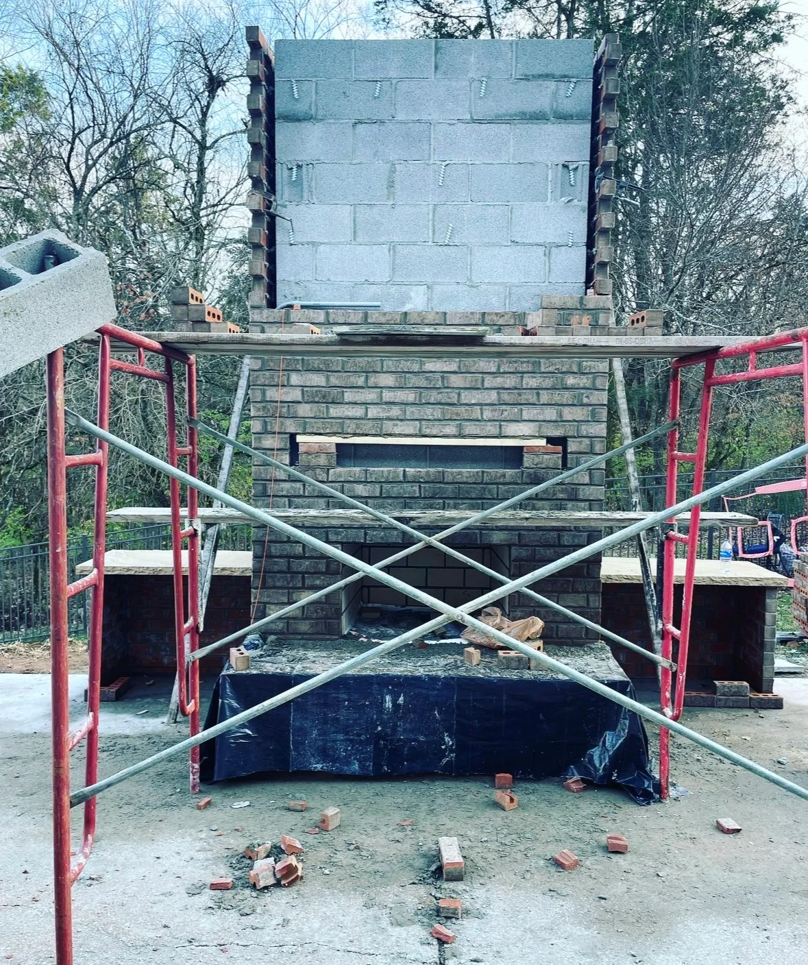 Outdoor fireplace under construction with red steel frame and concrete block chimney