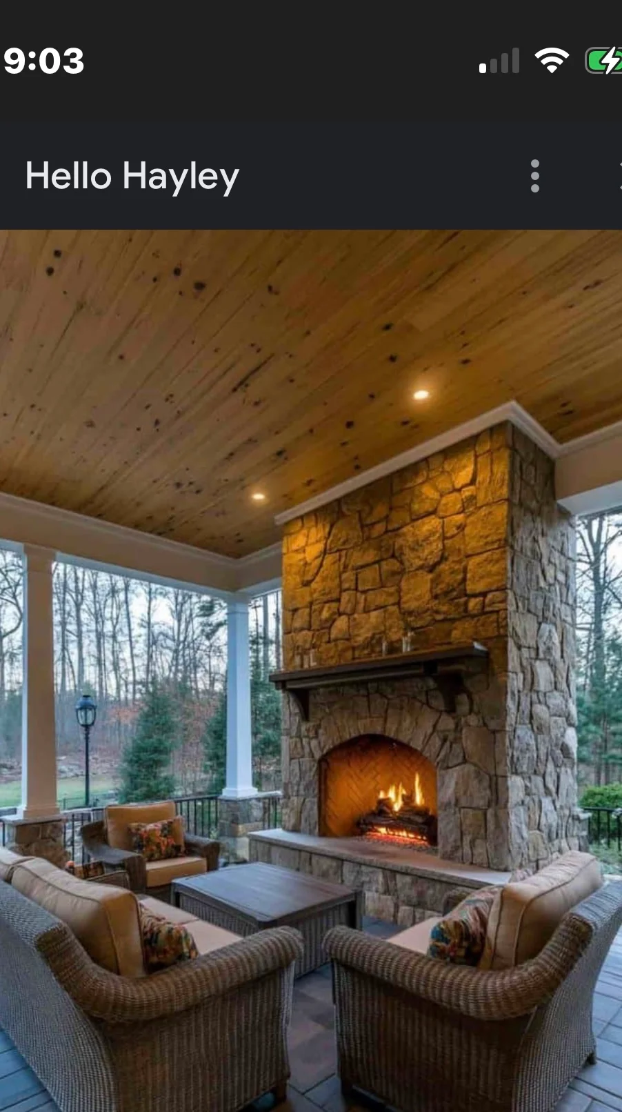 Stone fireplace with active fire on covered porch with pine ceiling and seating area
