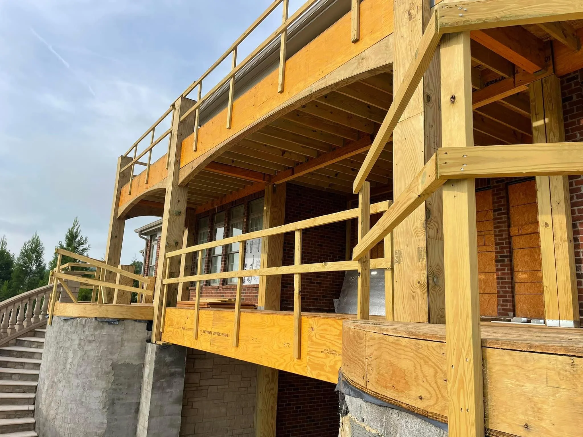 Two-story wooden deck under construction with yellow sheathing and metal railings on brick home